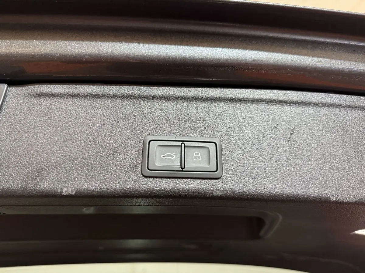 Boutons d'ouverture et de verrouillage du coffre sur le panneau intérieur du hayon d'une Audi A4 gris foncé, vue rapprochée.