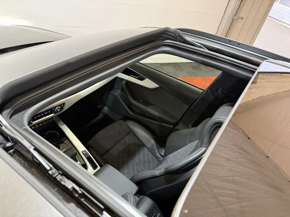 Vue intérieure par le toit ouvrant d'une Audi A4 gris foncé, montrant le siège avant droit et la console centrale.