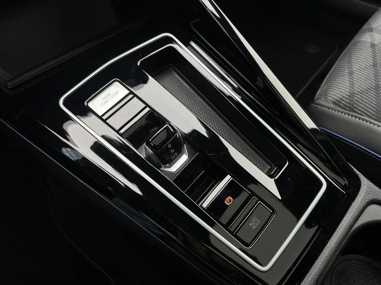 Vue rapprochée de la console centrale noire brillante de la Volkswagen Golf VIII avec sélecteur de vitesse DSG et boutons Start/Stop et frein électrique.