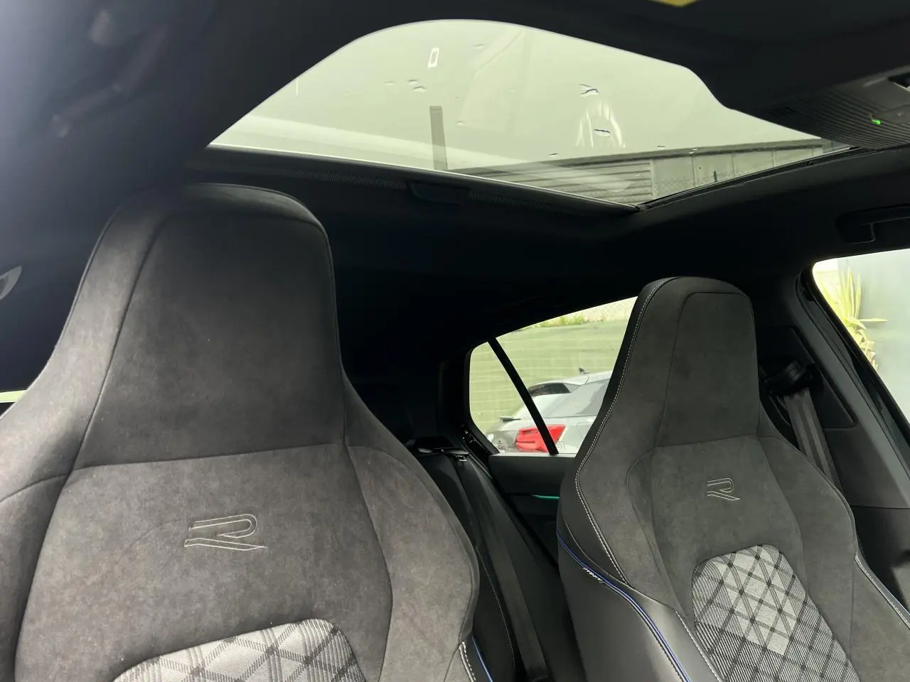 Vue intérieure montrant les sièges sport R-Line en alcantara gris avec toit ouvrant panoramique sur une Volkswagen Golf VIII noire.