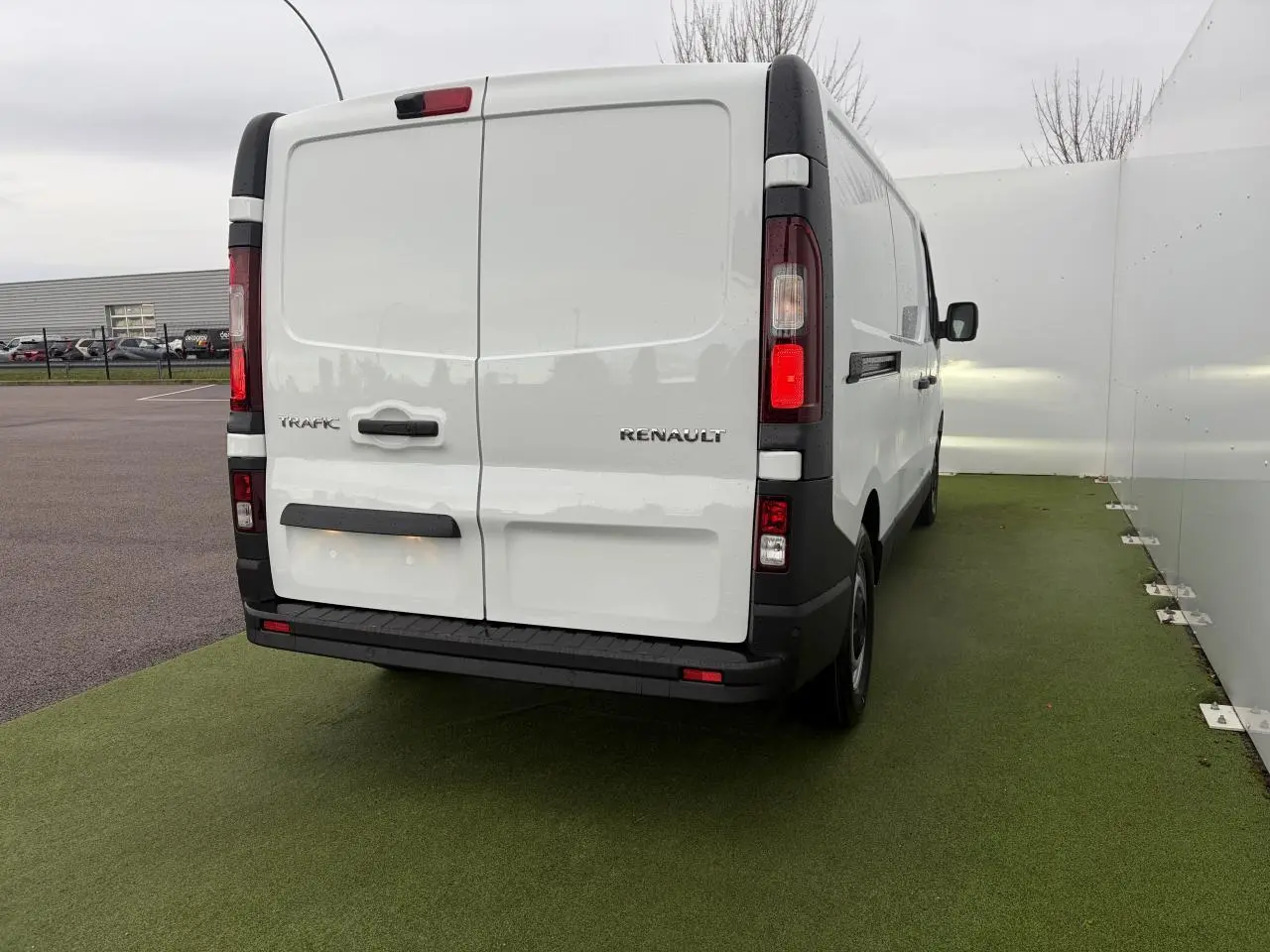 Vue arrière d’un Renault Trafic Fourgon blanc glacier, portes arrière tôlées ouvertes à 180°, feux verticaux rouges et blancs.