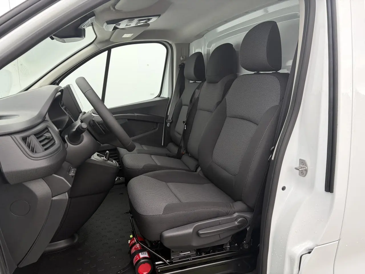 Vue intérieure côté conducteur du Renault Trafic Fourgon blanc glacier, montrant la banquette passager trois places en tissu gris.