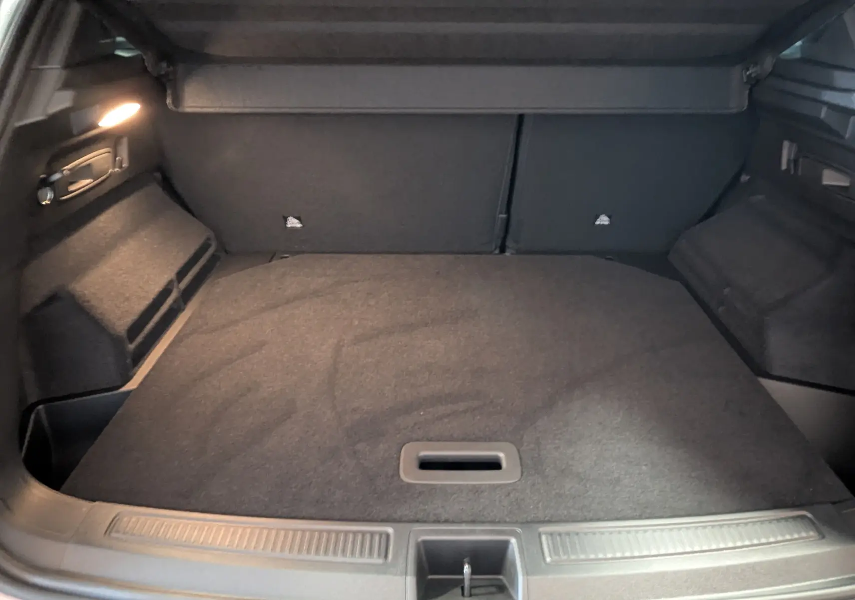 Coffre ouvert vu de l'arrière du Renault Austral E-Tech 200 gris schiste, avec tapis de sol et éclairage intérieur.