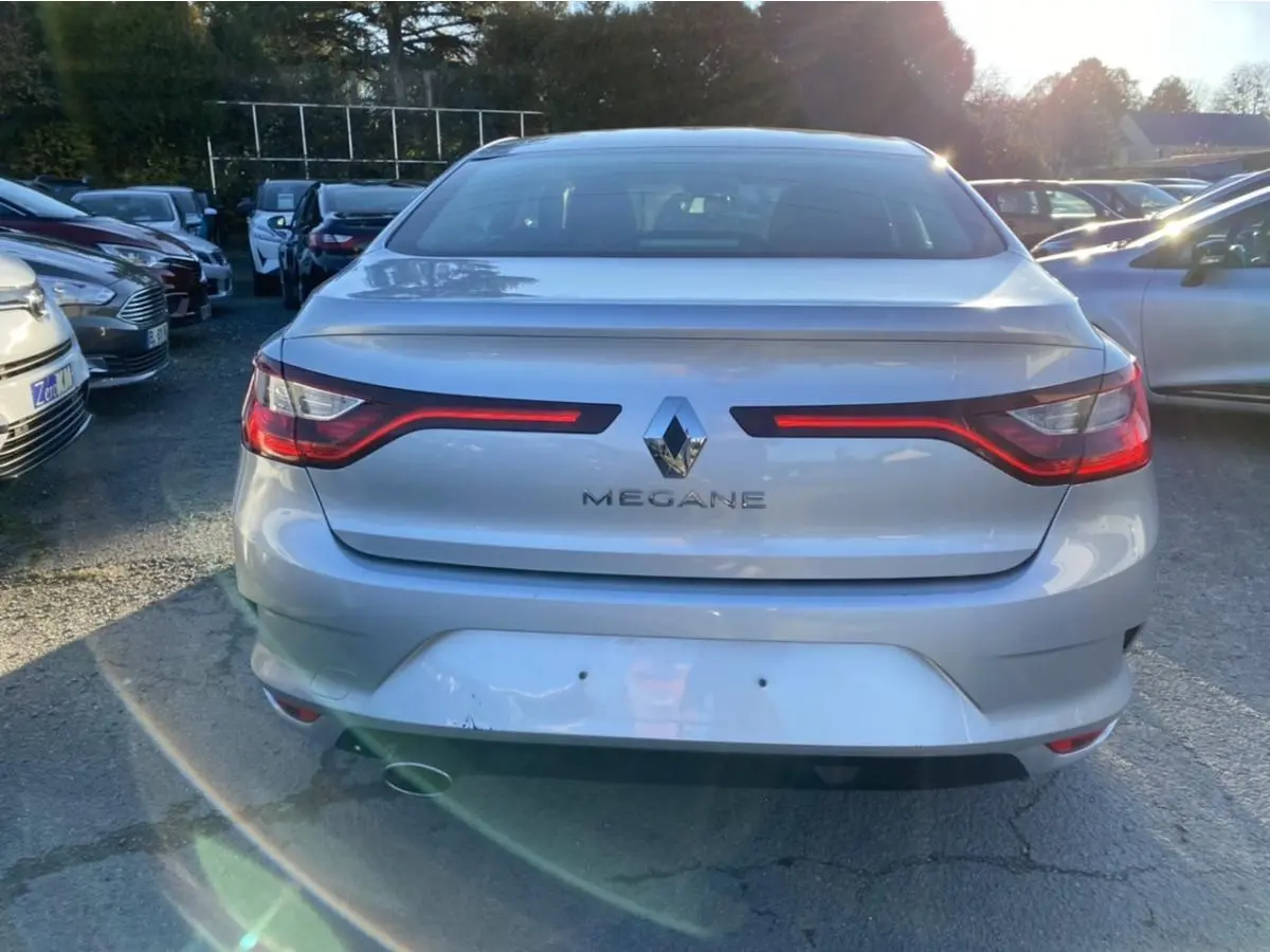 Vue arrière d'une Renault Mégane Sedan gris platine de 2017, avec feux arrière allumés et logo central visible.