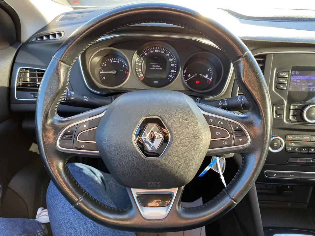 Vue rapprochée du volant en cuir noir de la Renault Mégane gris platine, avec tableau de bord et console centrale visibles.