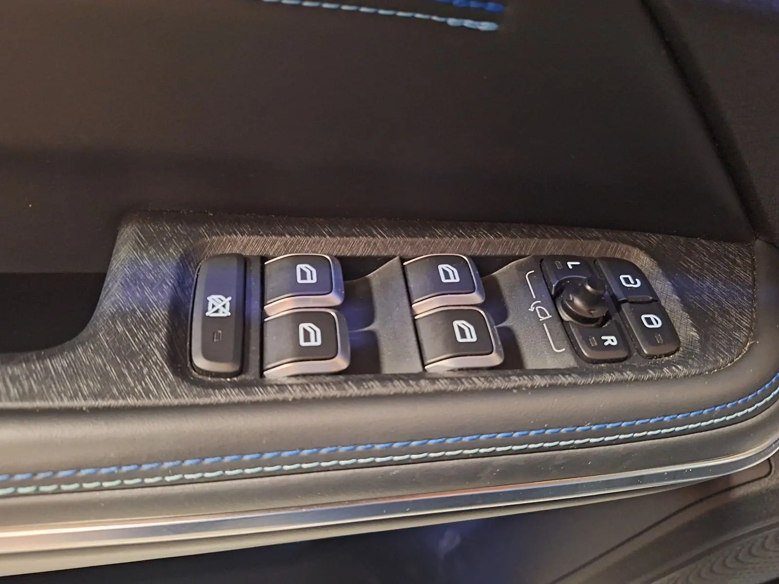 Gros plan sur les commandes des vitres et rétroviseurs côté gauche d’un LYNK & CO 01 noir avec surpiqûres bleues.