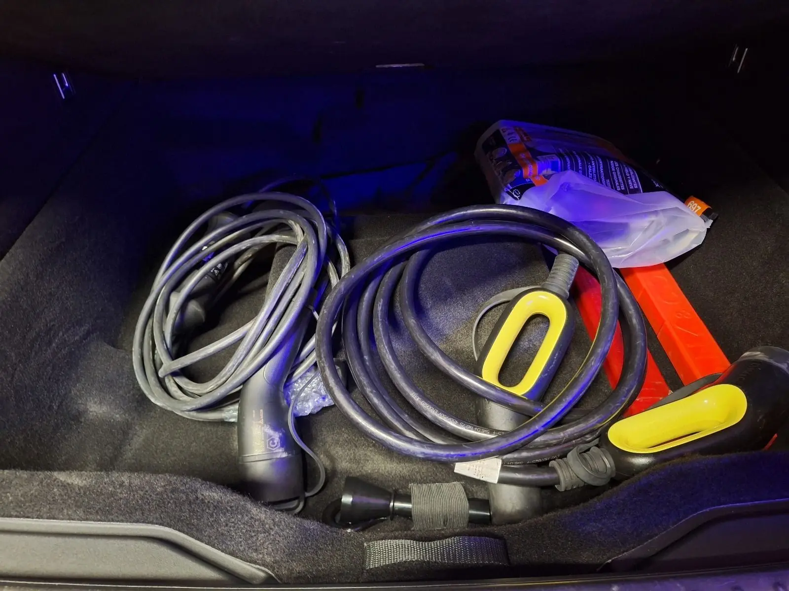 Coffre d’un Lynk & Co 01 noir 2023 montrant câbles de recharge hybride et triangle de signalisation rouge.