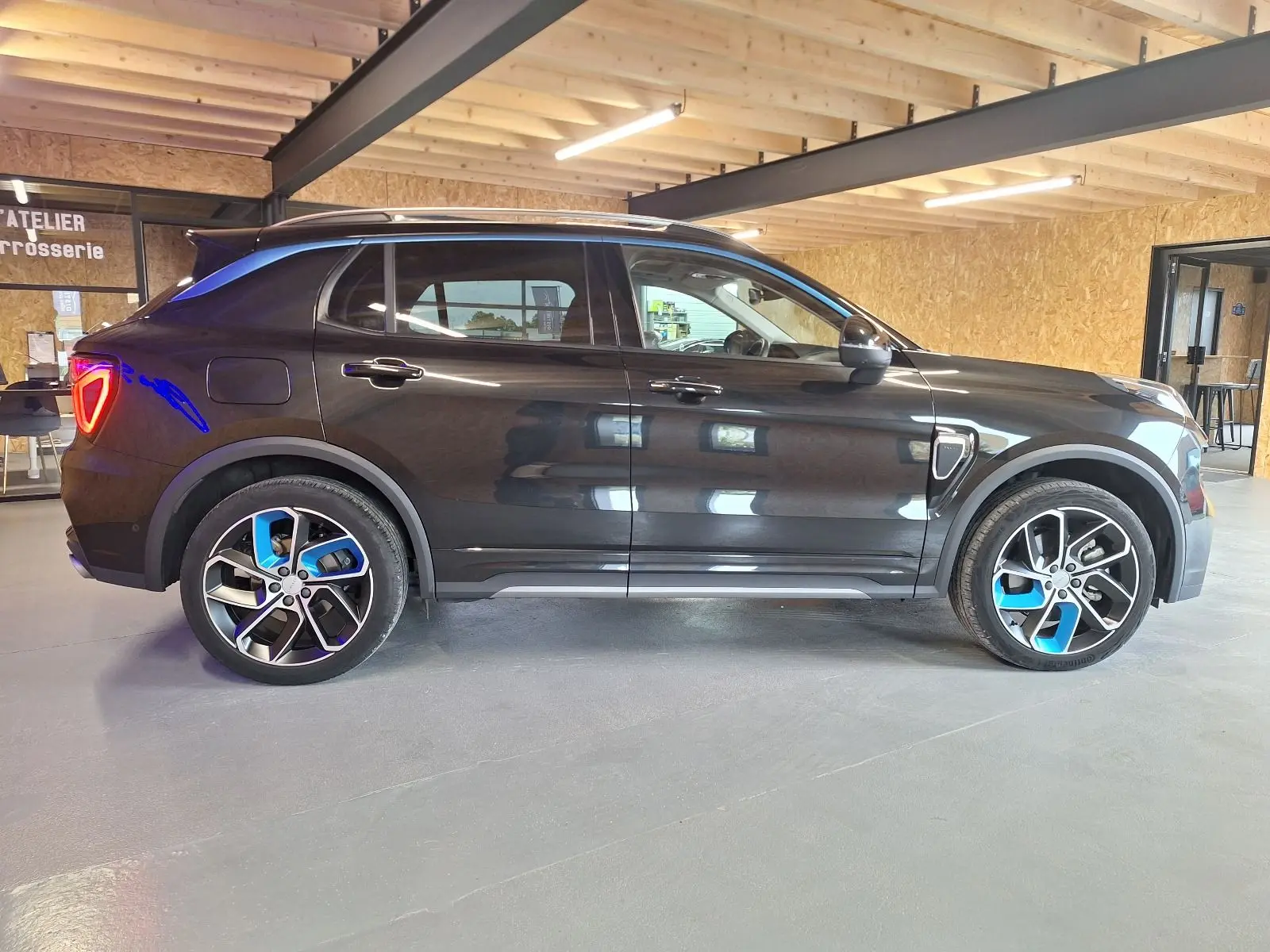 Vue latérale droite d'un LYNK & CO 01 noir 2023 avec jantes bicolores et feux arrière allumés en intérieur.