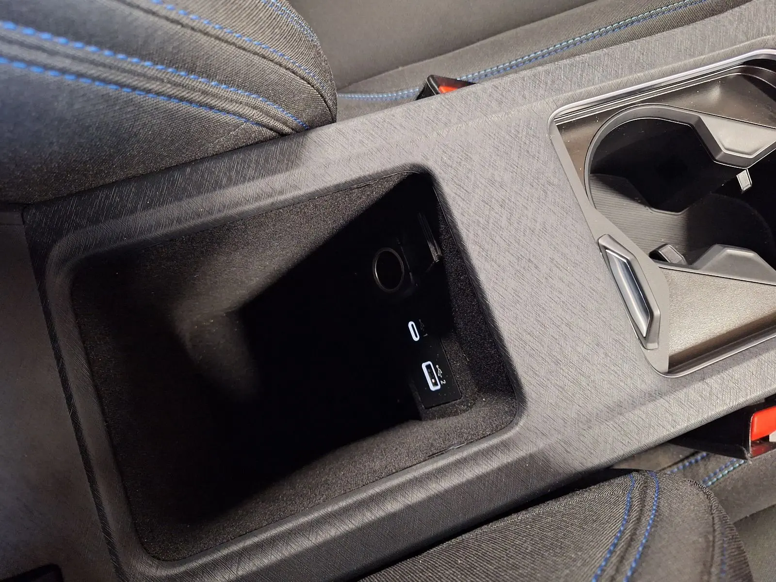 Gros plan sur la console centrale noire du Lynk & Co 01 avec prises USB et tissu noir aux surpiqûres bleues.