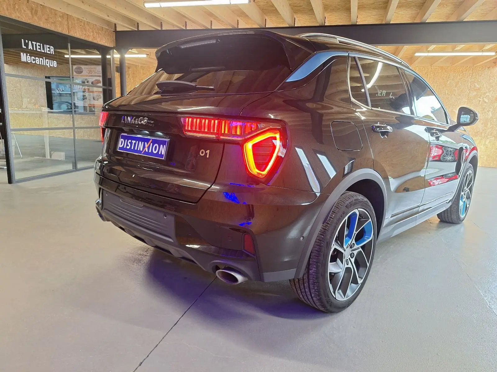 Vue 3/4 arrière droite d'un SUV LYNK & CO 01 noir avec feux arrière allumés et jantes bicolores en intérieur d'atelier.