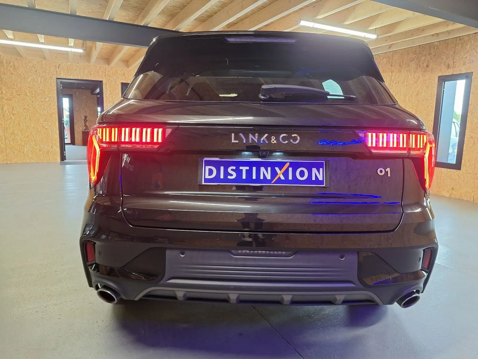 Vue arrière d'un SUV LYNK & CO 01 noir avec feux LED allumés dans un garage lumineux.