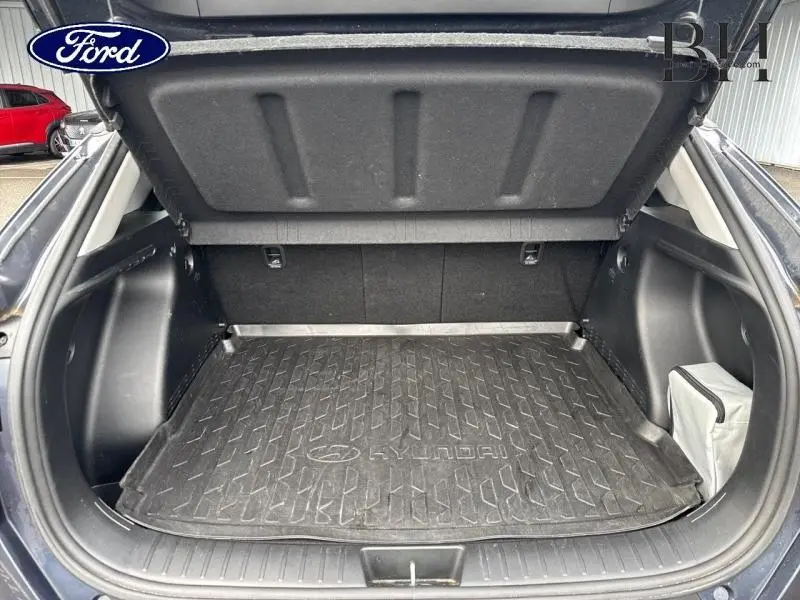 Coffre ouvert vu de l'arrière d'un Hyundai Kona Denim Blue avec tapis de coffre en caoutchouc marqué Hyundai.