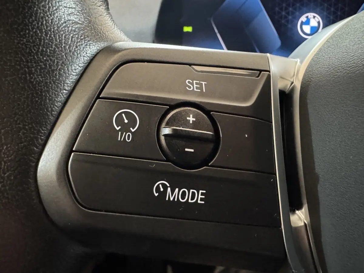 Gros plan sur les commandes de régulateur de vitesse au volant cuir du BMW X1 gris foncé 2024.