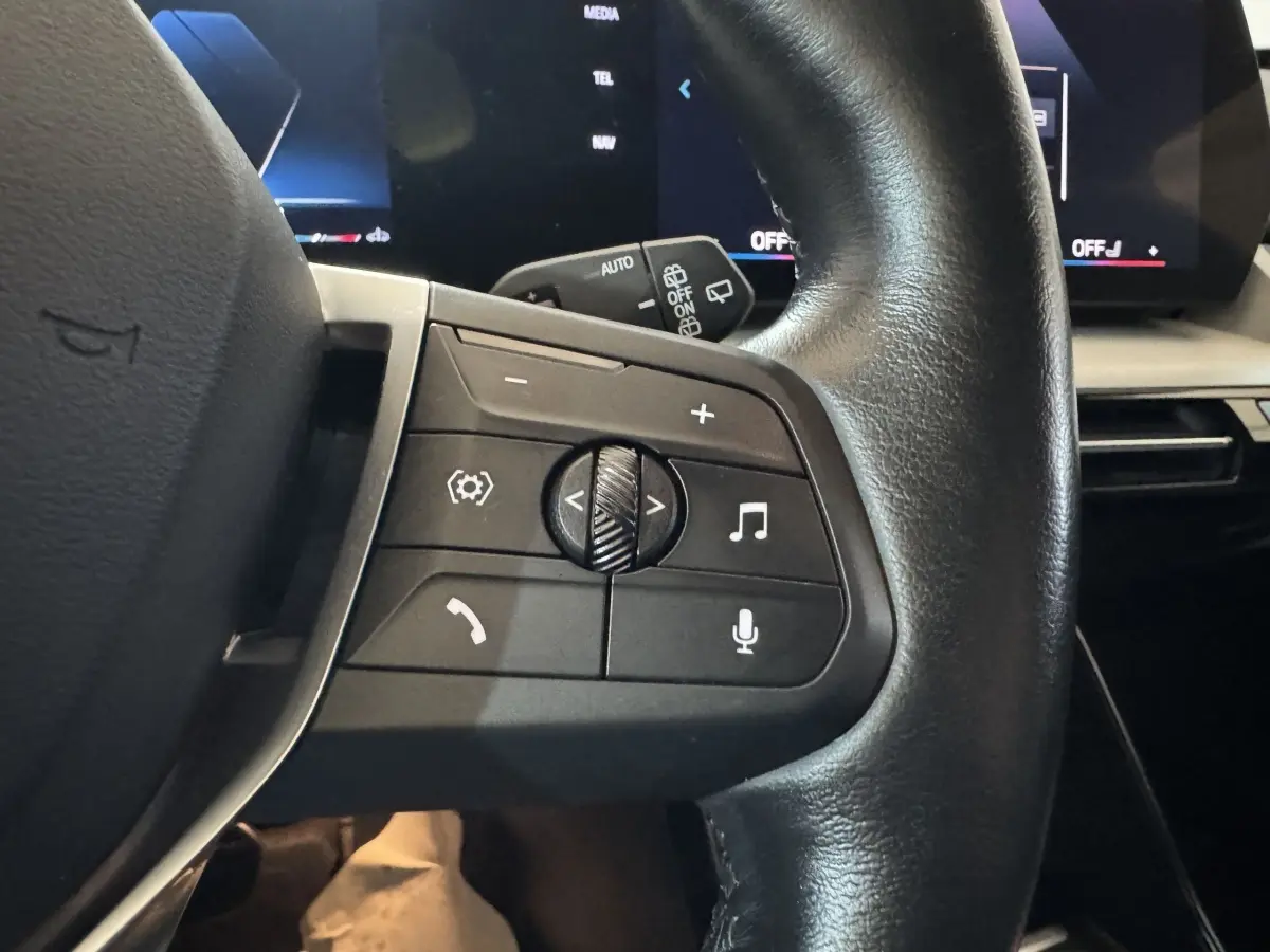 Gros plan sur le volant cuir noir du BMW X1 2024, côté gauche, avec commandes audio et vocales visibles.
