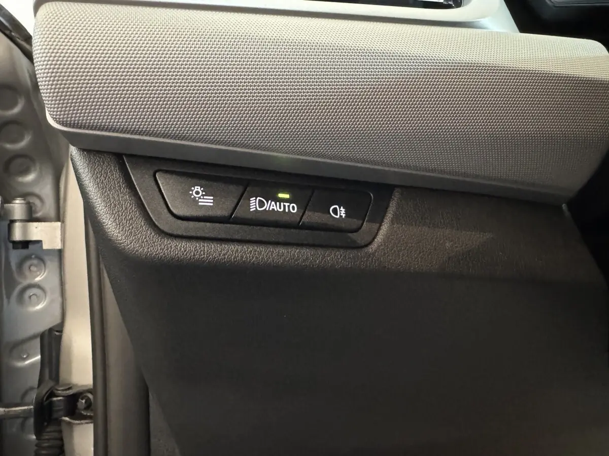 Gros plan sur les commandes d’éclairage automatiques et antibrouillard à gauche du tableau de bord d’une BMW X1 gris foncé 2024.