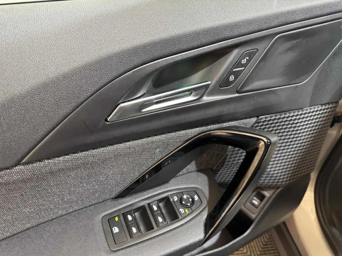 Gros plan sur la porte côté conducteur de la BMW X1 2024 gris foncé, avec commandes de vitres et verrouillage.