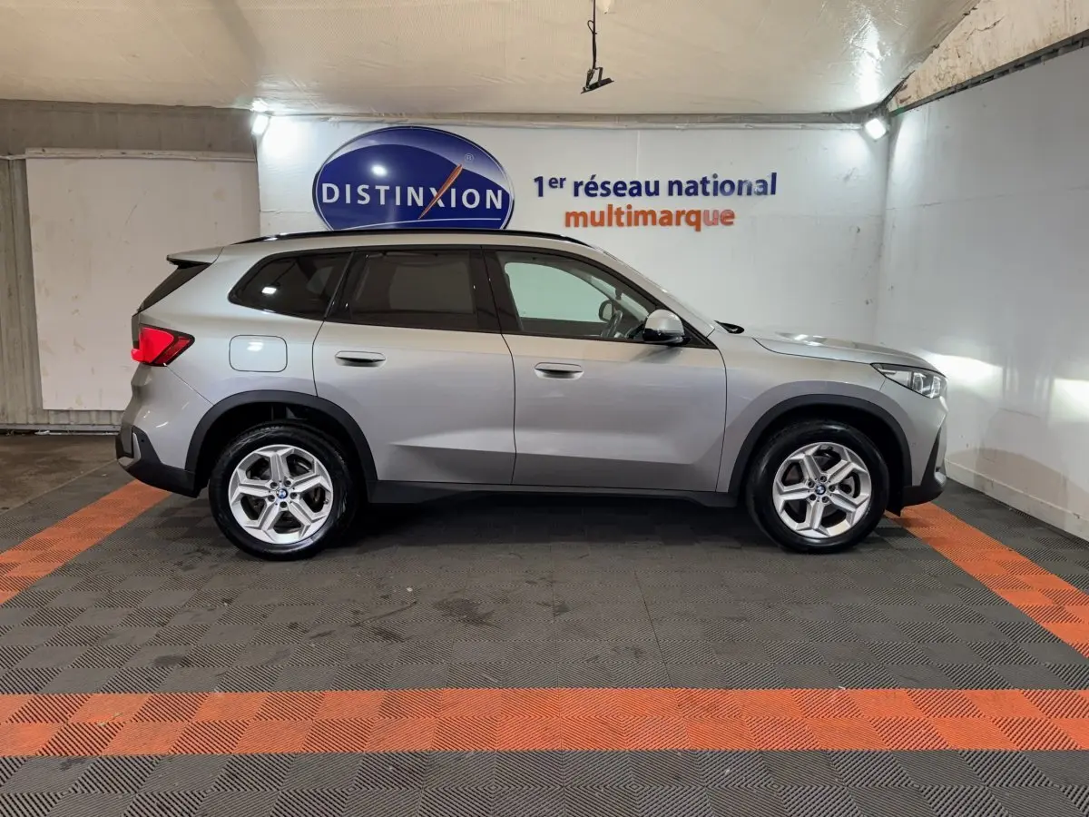 Vue de profil côté gauche d’un BMW X1 sDrive20i Business Design gris foncé dans un showroom intérieur.