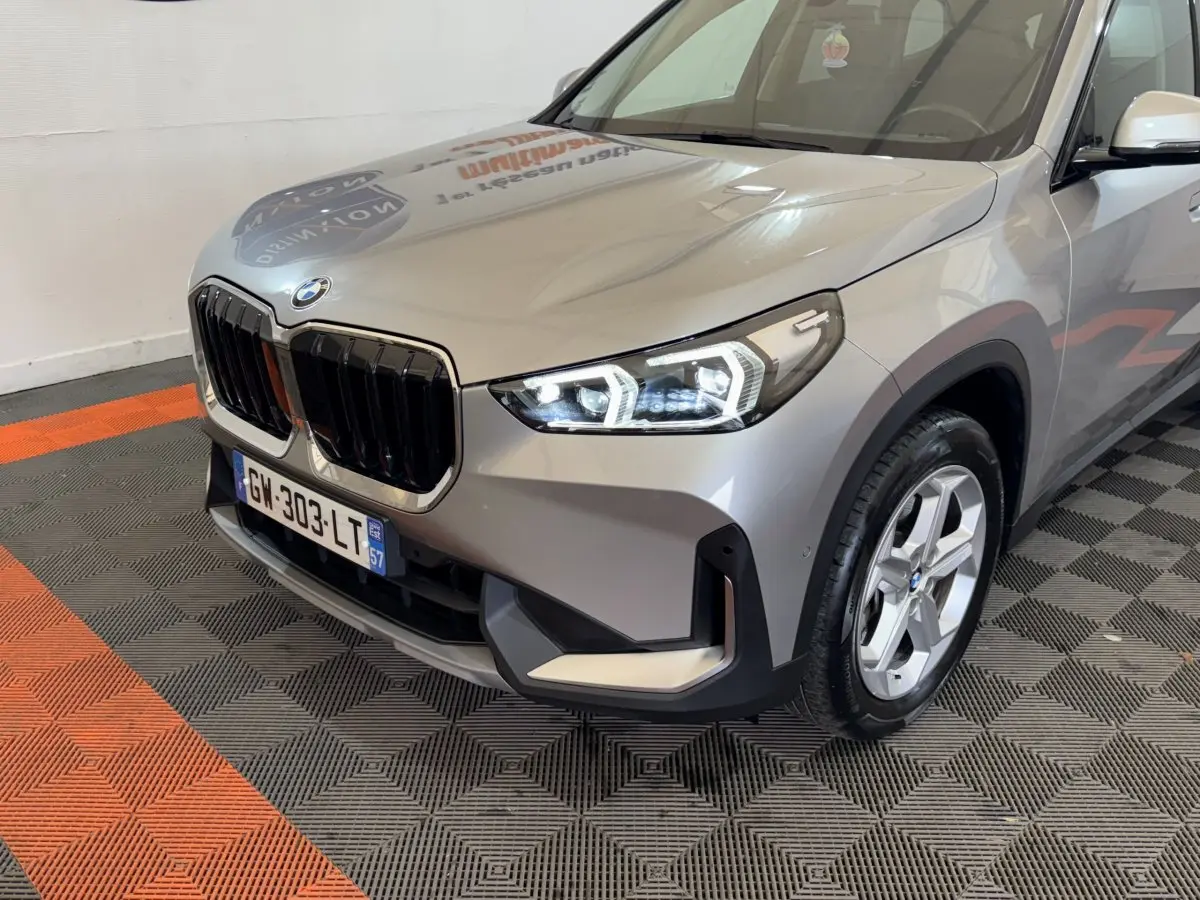 BMW X1 sDrive20i gris foncé vue 3/4 avant droit, avec calandre noire et phares LED allumés.