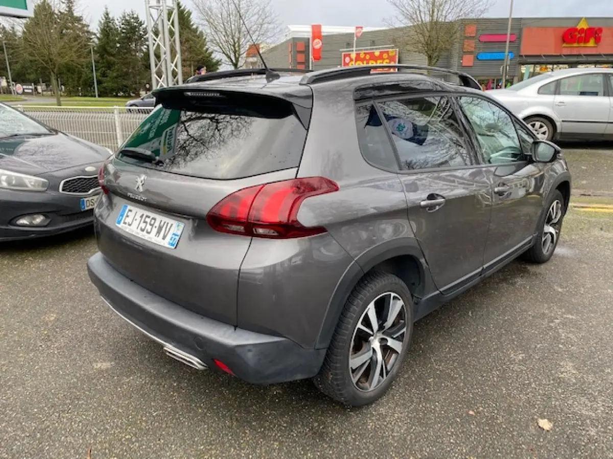 Peugeot 2008 gris platinium en 3/4 arrière droit, avec barres de toit noir brillant et jantes alliage 17 pouces.