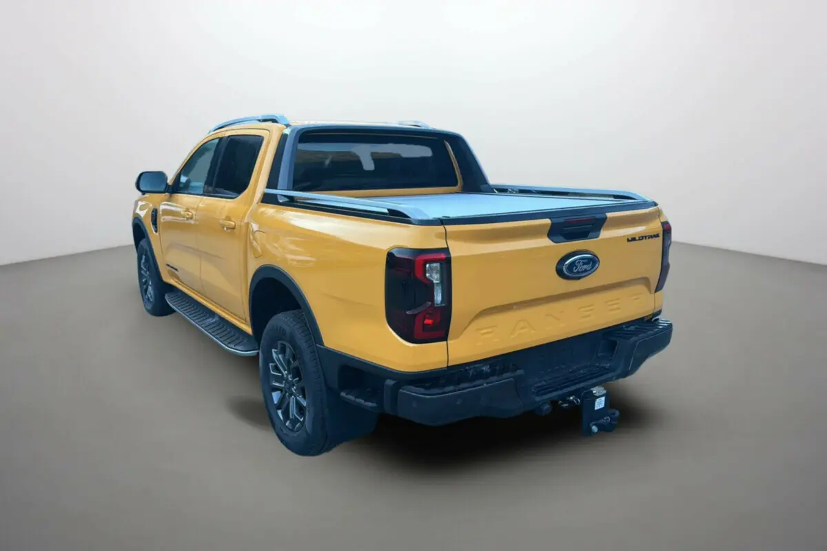 Ford Ranger 2.3 PHEV Wildtrak Plus 2026 en Cyber orange, vue 3/4 arrière droite avec attelage et barres de toit.