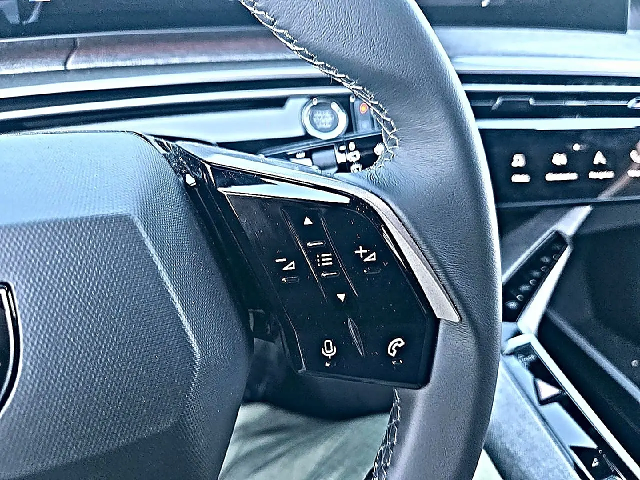 Gros plan sur le volant cuir noir multifonction du Peugeot 5008 blanc, avec commandes vocales et audio visibles.