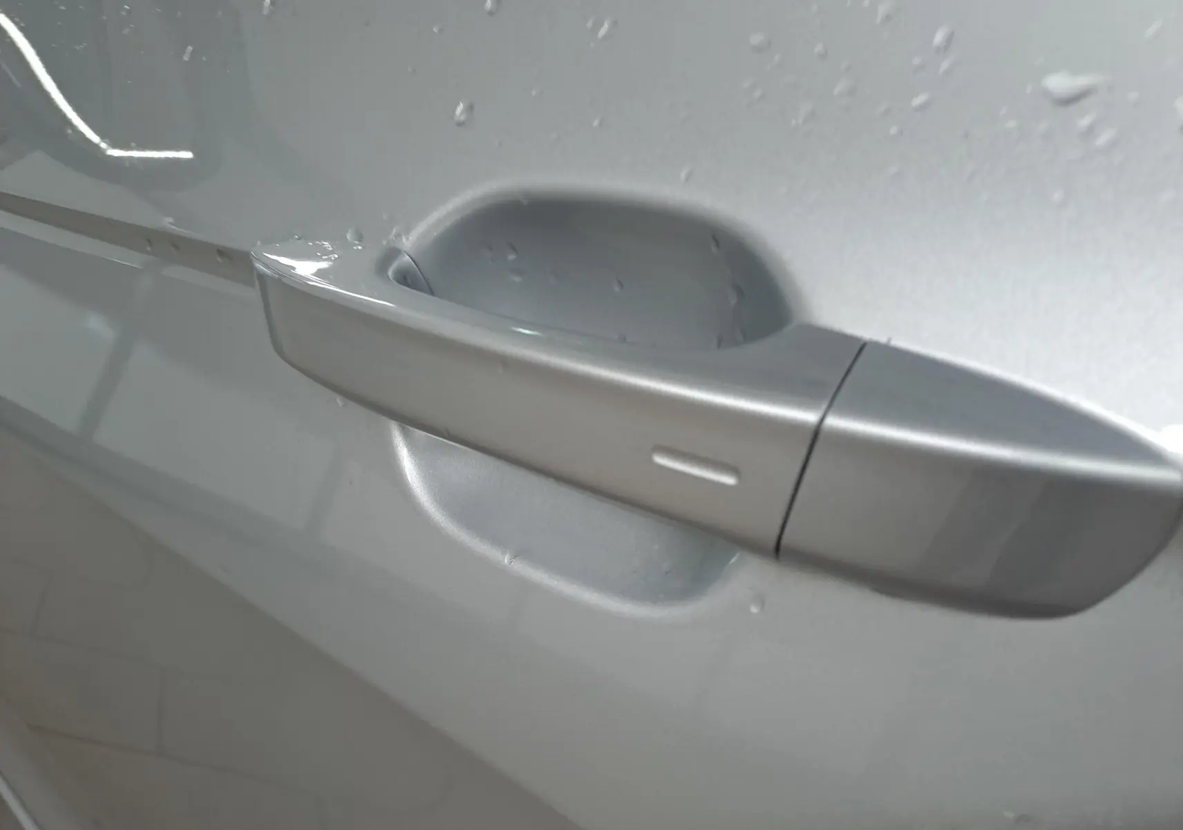 Poignée de porte côté gauche du Volkswagen T-Cross 2025 R-Line Edition en Reflet d'argent avec gouttes d'eau visibles.