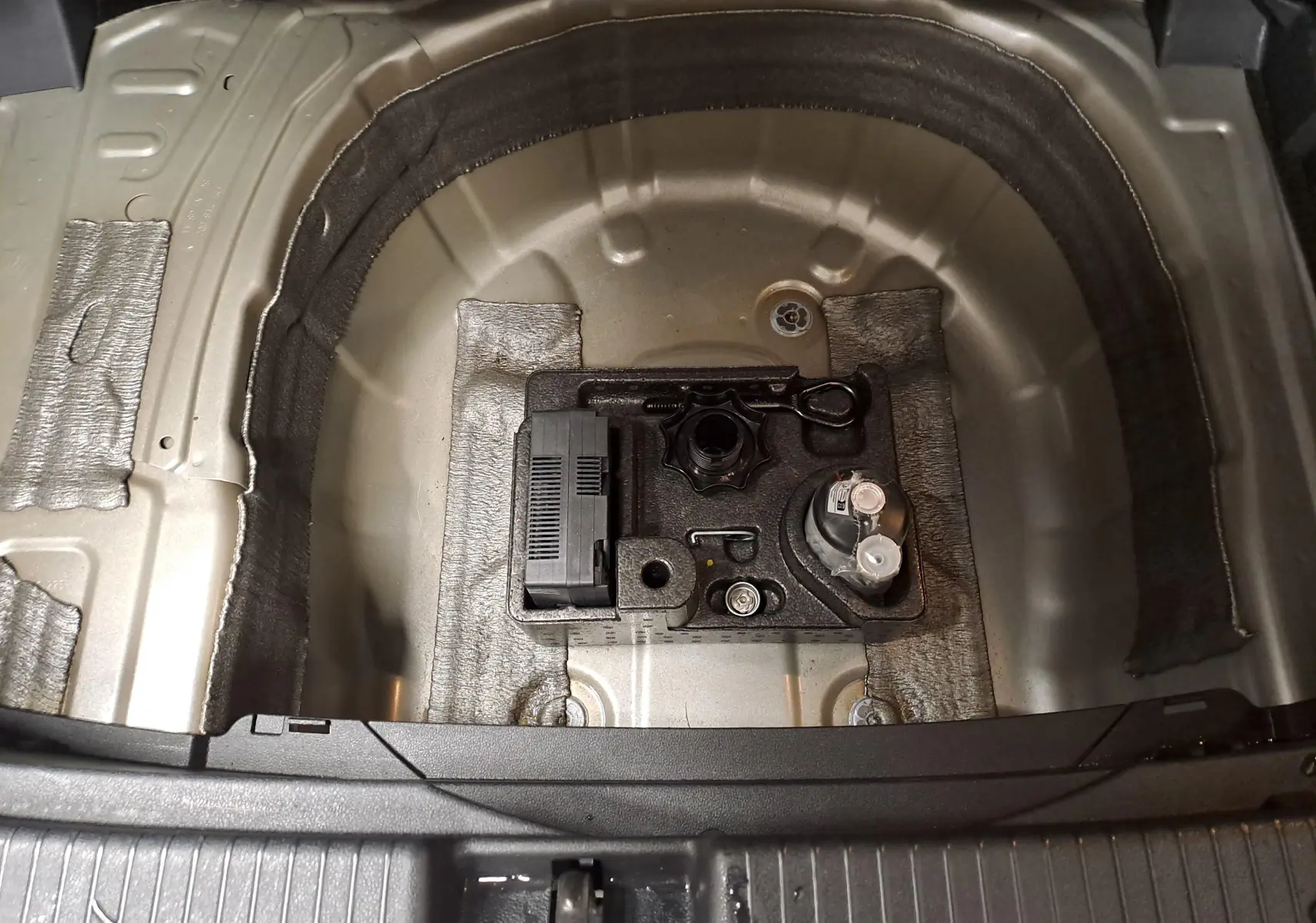 Vue plongeante sur le coffre ouvert du Volkswagen T-Cross 2025 argent, montrant le logement de la roue de secours vide et ses outils.