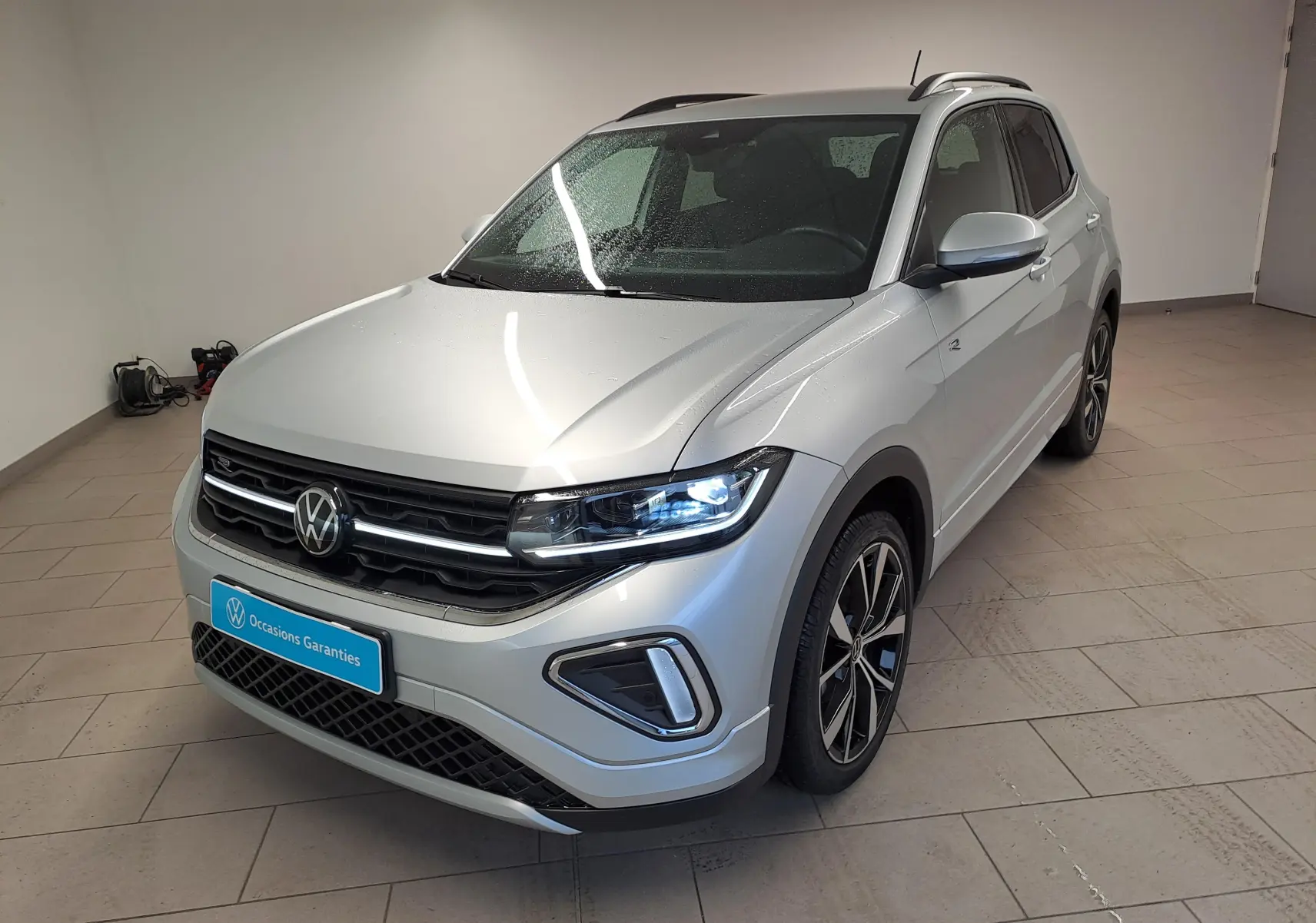 Volkswagen T-Cross 2025 Reflet d'argent en 3/4 avant droit avec phares LED allumés et jantes R-Line noires.