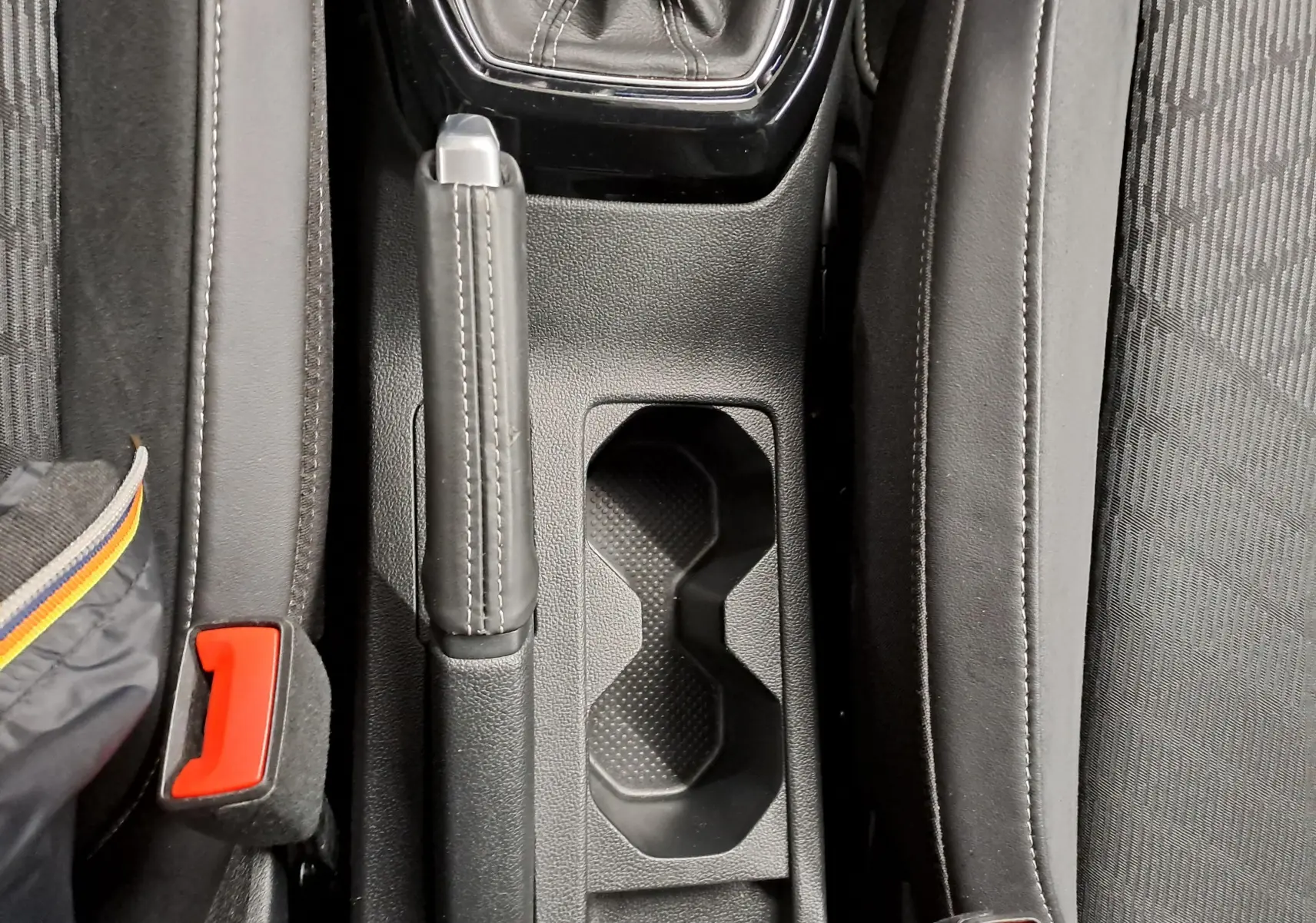 Vue plongeante sur la console centrale noire du Volkswagen T-Cross 2025, avec frein à main et porte-gobelets.