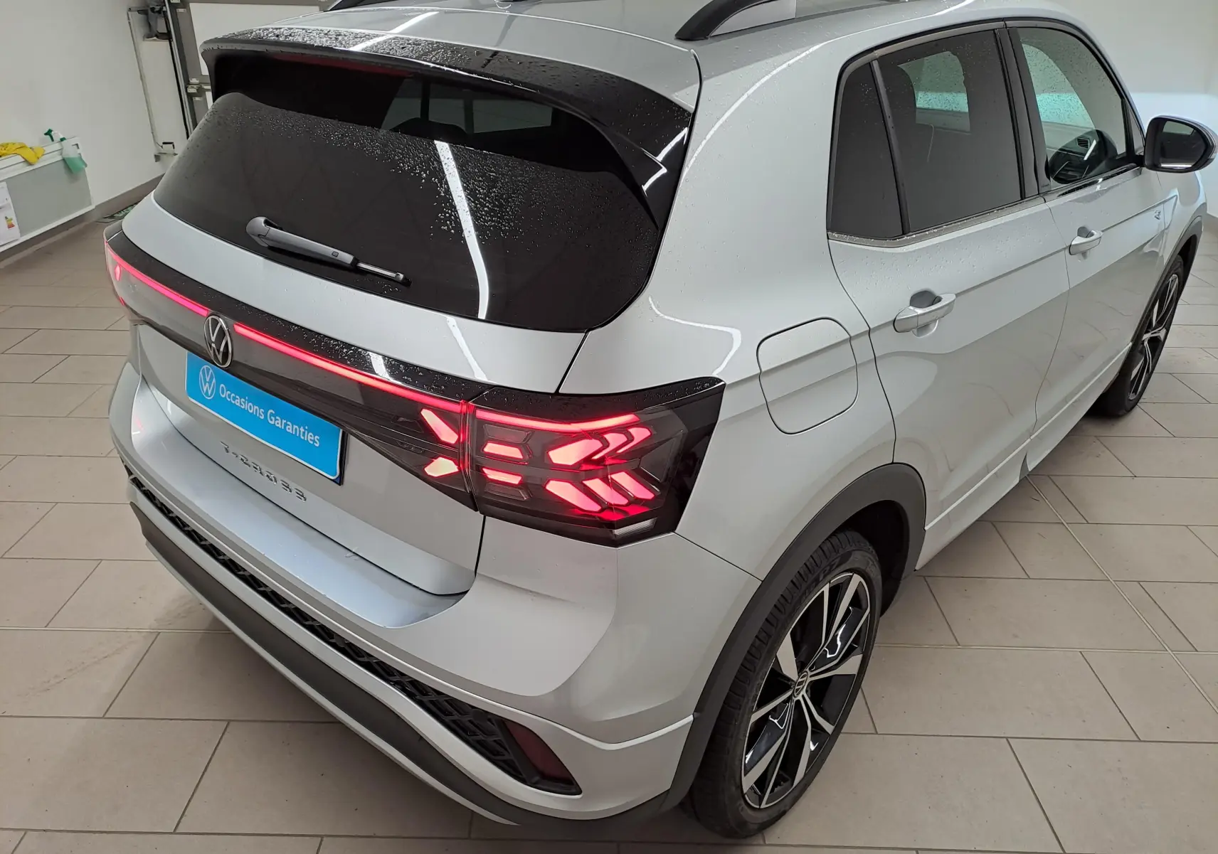 Vue 3/4 arrière droite d’un Volkswagen T-Cross 2025 R-Line Edition en Reflet d’argent avec feux arrière LED allumés.