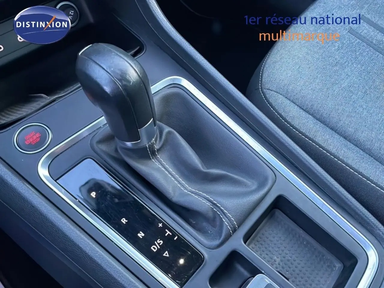 Gros plan sur la console centrale avec levier de vitesse automatique en cuir noir et siège tissu gris à droite.