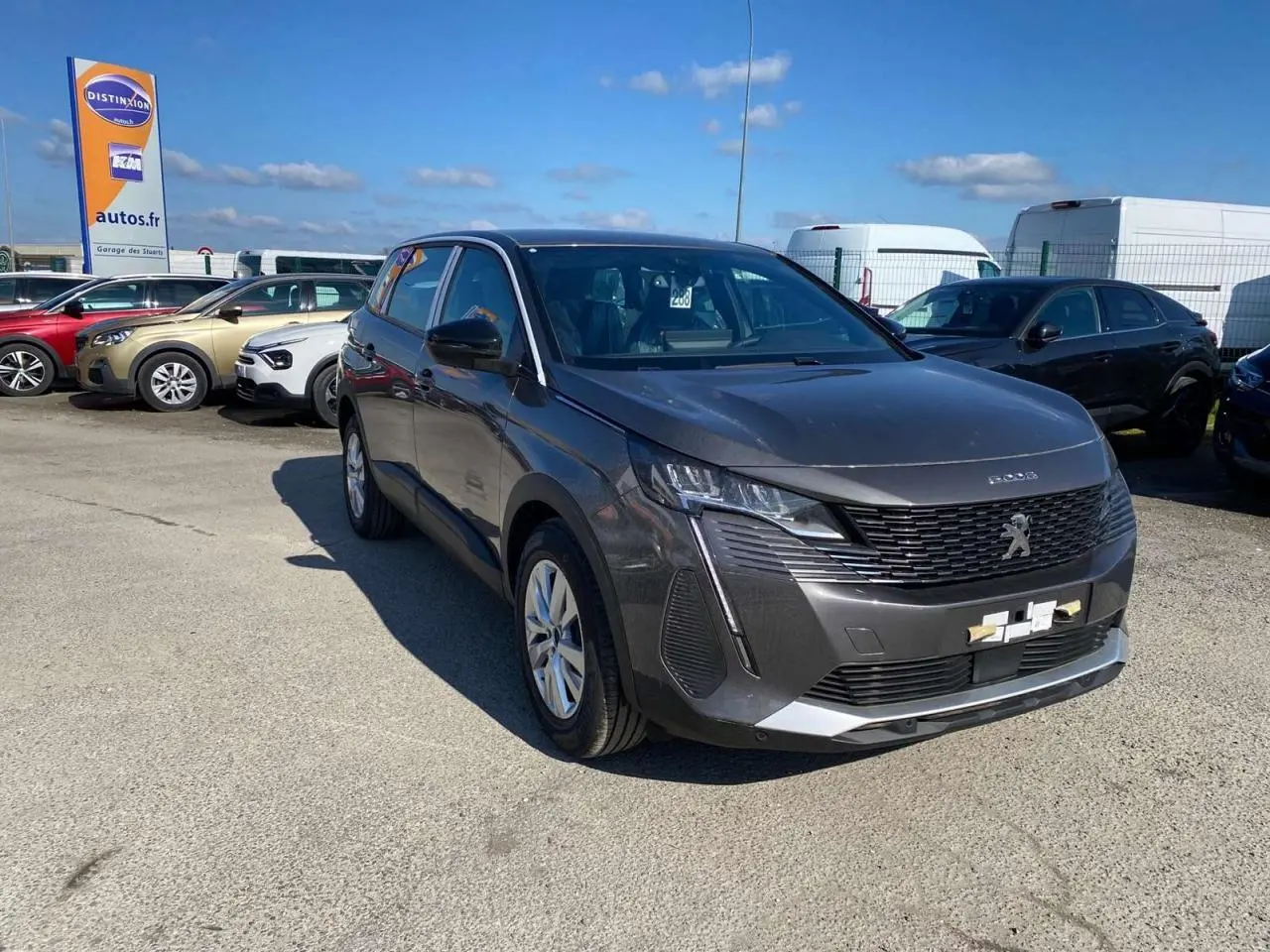 Peugeot 5008 gris platinium métal vue 3/4 avant droit sur parking sous ciel bleu.