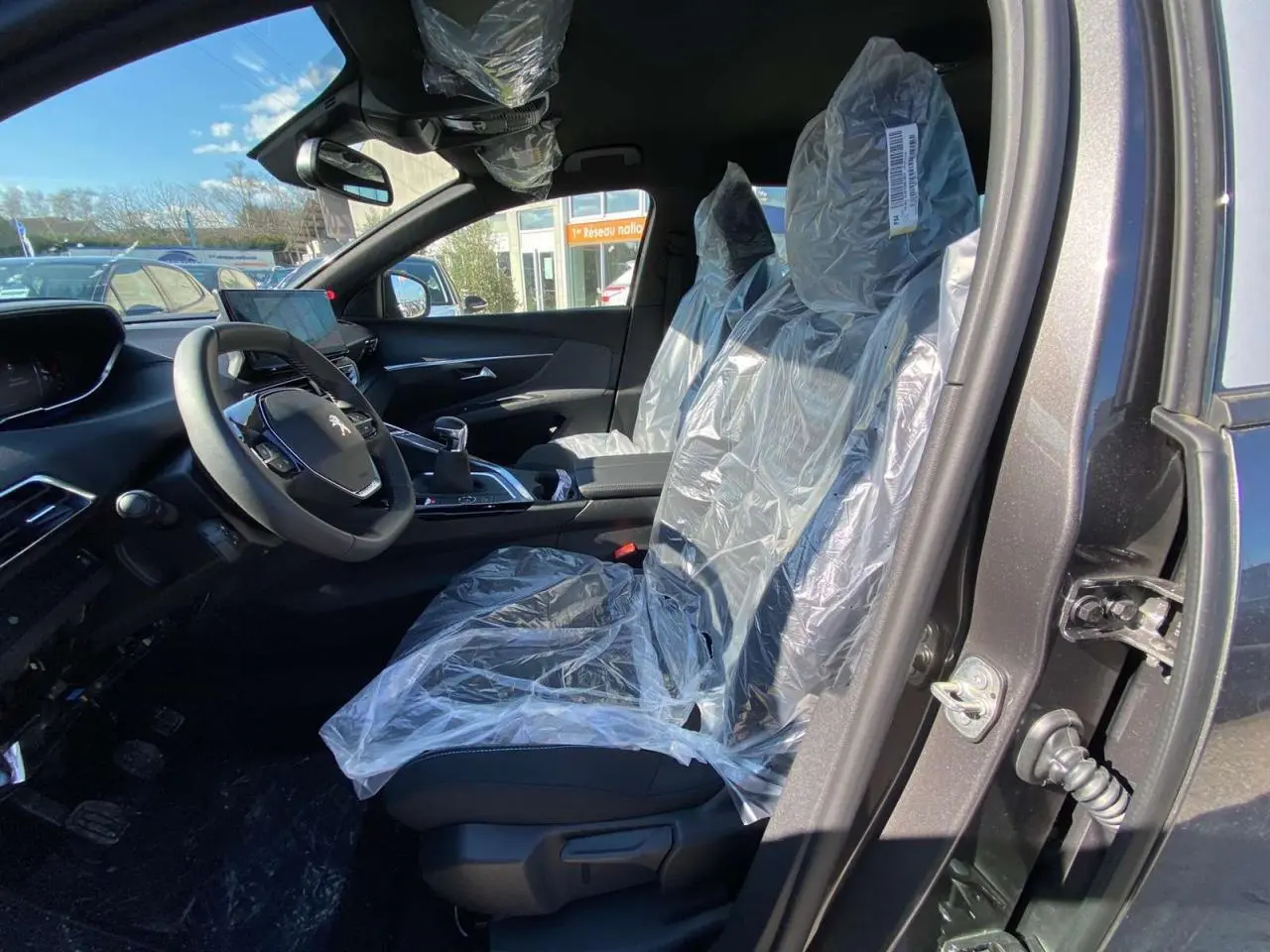 Vue intérieure côté conducteur du Peugeot 5008 gris platinium, sièges avant protégés par housses plastiques.