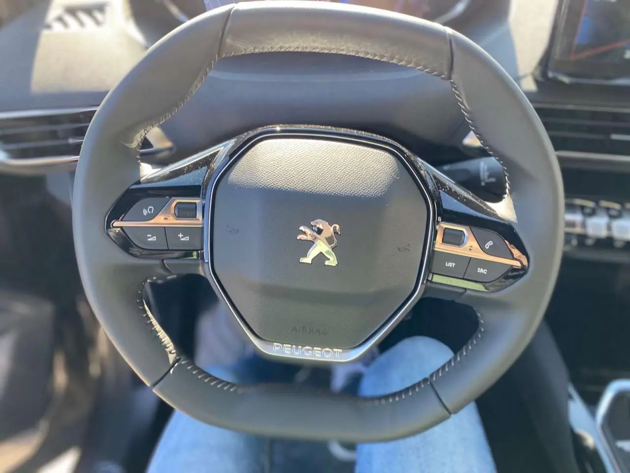 Gros plan sur le volant compact multifonctions noir du Peugeot 5008 avec logo lion chromé au centre.