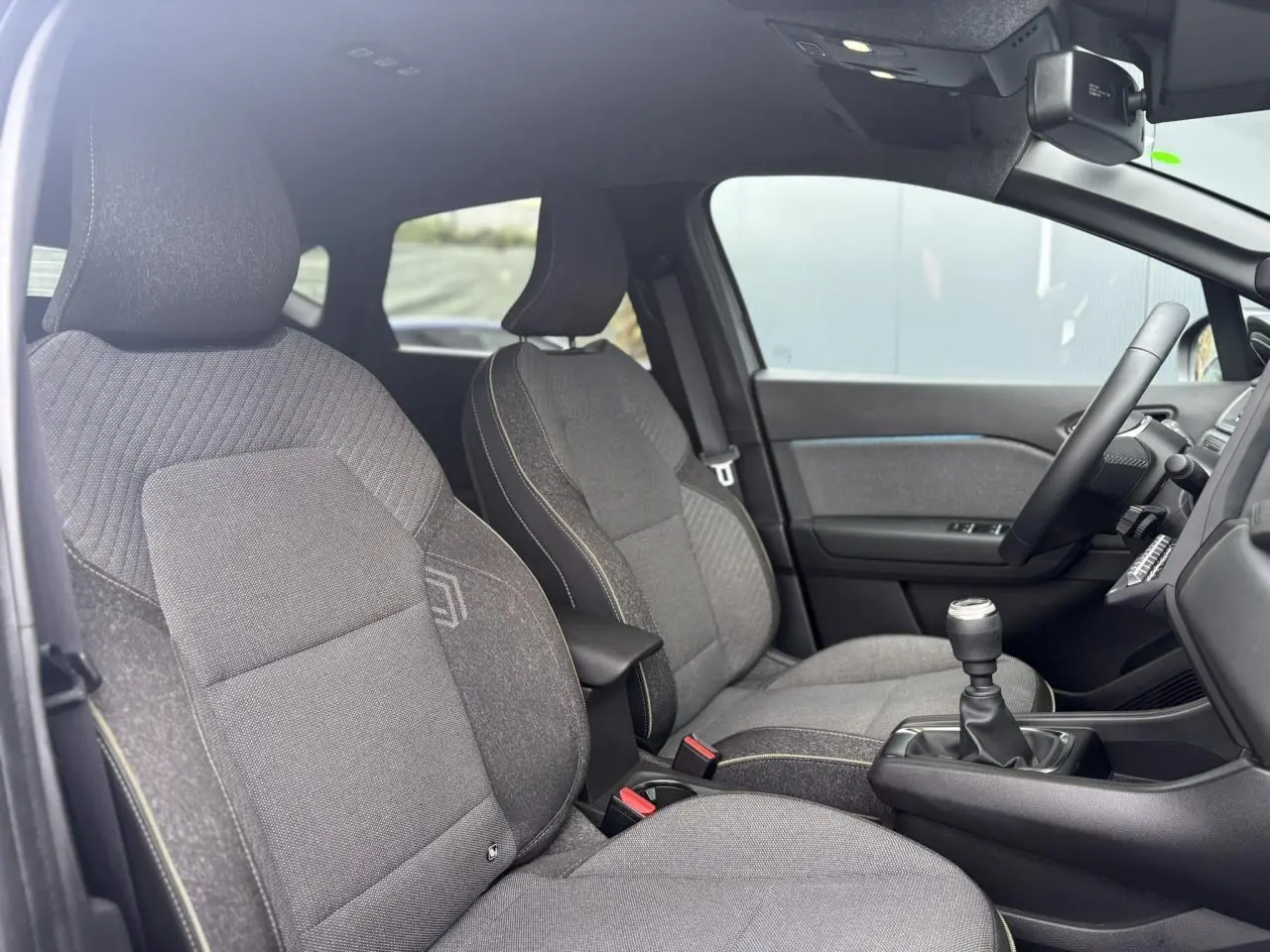 Vue intérieure côté conducteur du Renault Captur TCE 100 Techno 2025, sièges gris et levier de vitesse manuel visible.