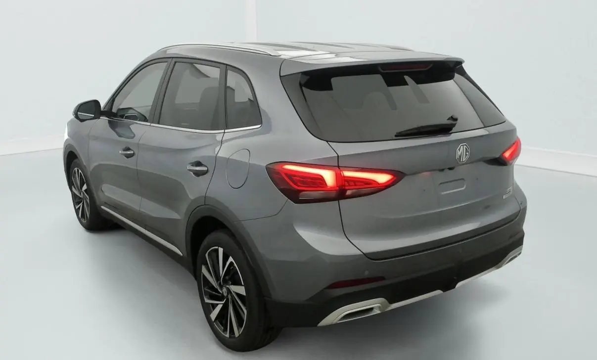 Vue 3/4 arrière gauche de la MG3 1.5 L HYBRID+ 195 CH Luxury en blanc Dover avec feux arrière allumés et jantes noires.