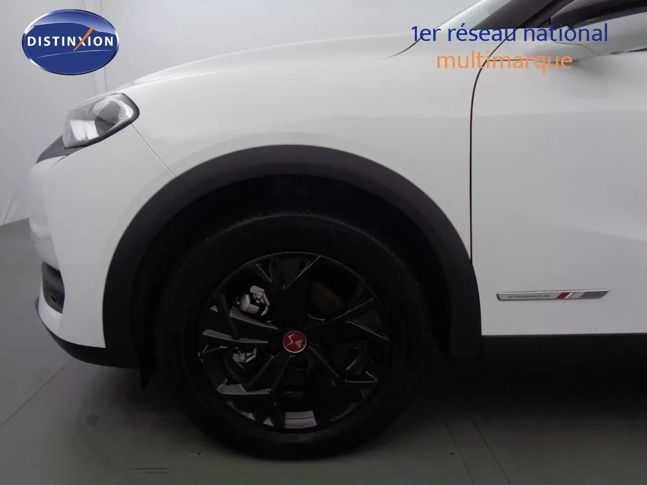 Gros plan sur la roue avant gauche noire et la carrosserie blanche banquise du DS3 Crossback 1.5 BlueHDi 130 Performance Line.