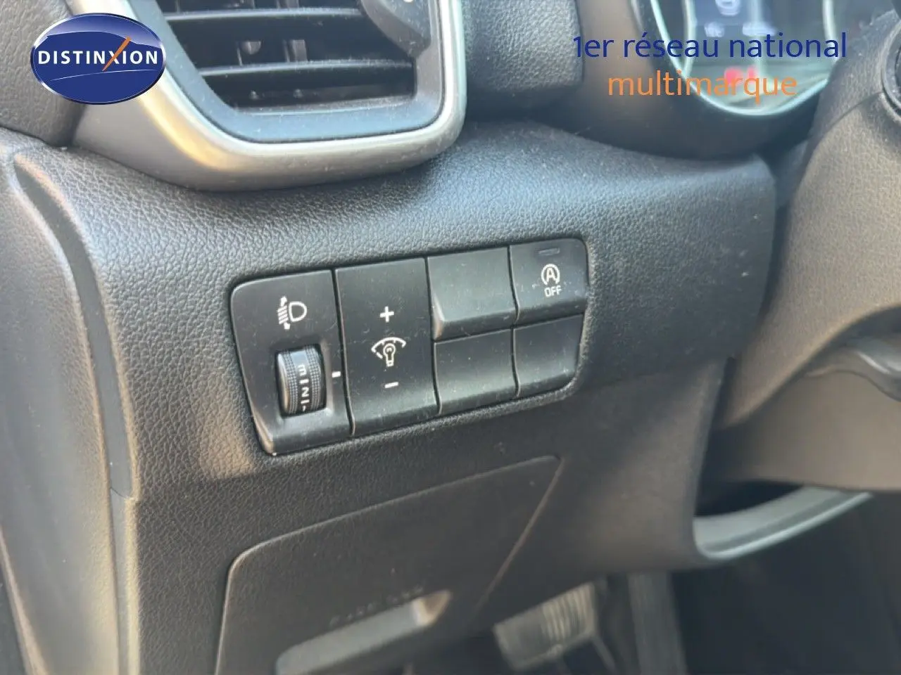 Gros plan sur les commandes de réglage des phares et désactivation du système start-stop dans un Kia Sportage blanc nacré 2021.