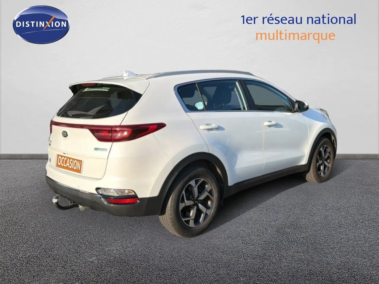 Vue 3/4 arrière droite du Kia Sportage blanc nacré avec jantes alliage bicolores et attelage visible.