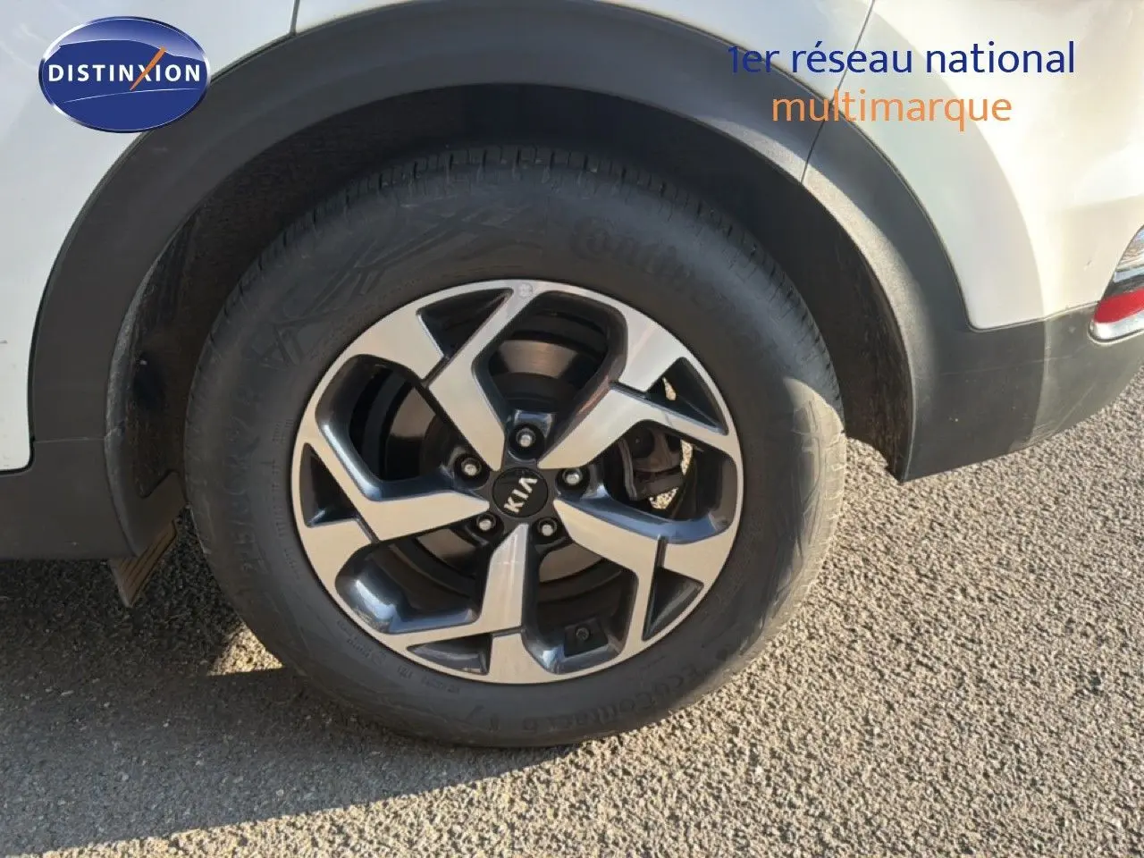 Gros plan sur la roue arrière droite d’un Kia Sportage blanc nacré avec jante alliage 5 branches bicolore.