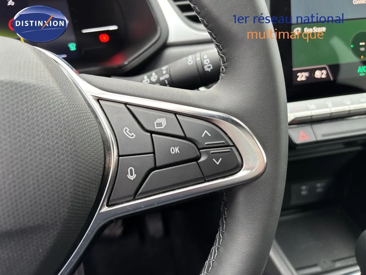 Gros plan sur les commandes multifonctions à droite du volant noir du Renault Symbioz blanc nacré, avec tableau de bord digital en arrière-plan.