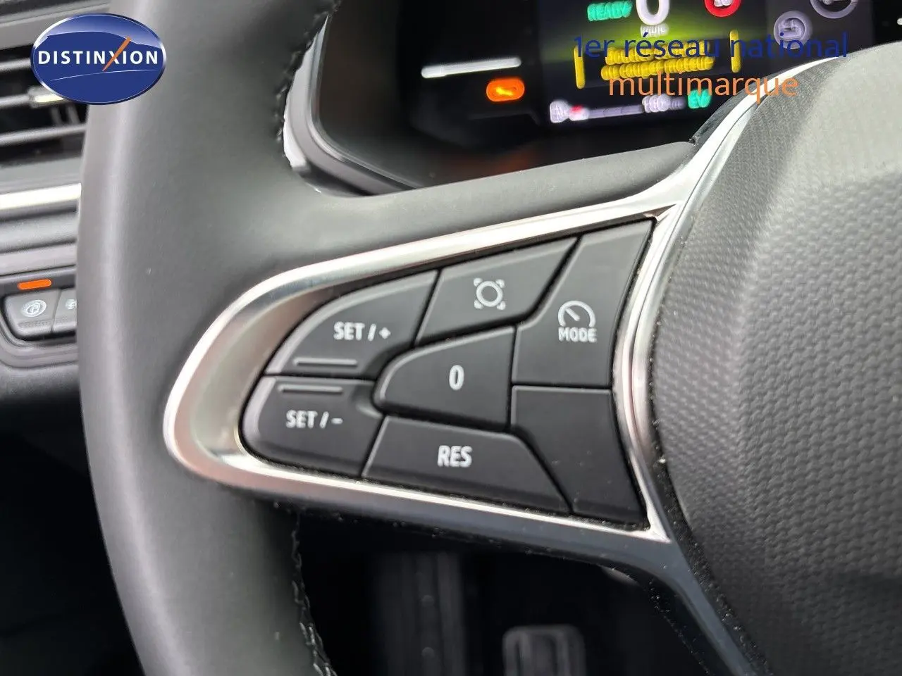Gros plan sur les commandes à gauche du volant du Renault Symbioz blanc nacré, affichage numérique en arrière-plan.