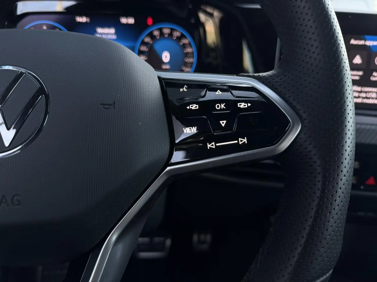 Gros plan sur le volant cuir perforé de la Volkswagen Golf 8 R-Line 2024 avec commandes multifonctions et affichage digital bleu.