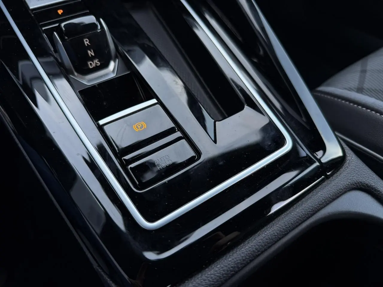 Gros plan sur la console centrale noire brillante avec levier de vitesse automatique et frein de stationnement électrique d’une Volkswagen Golf VIII.