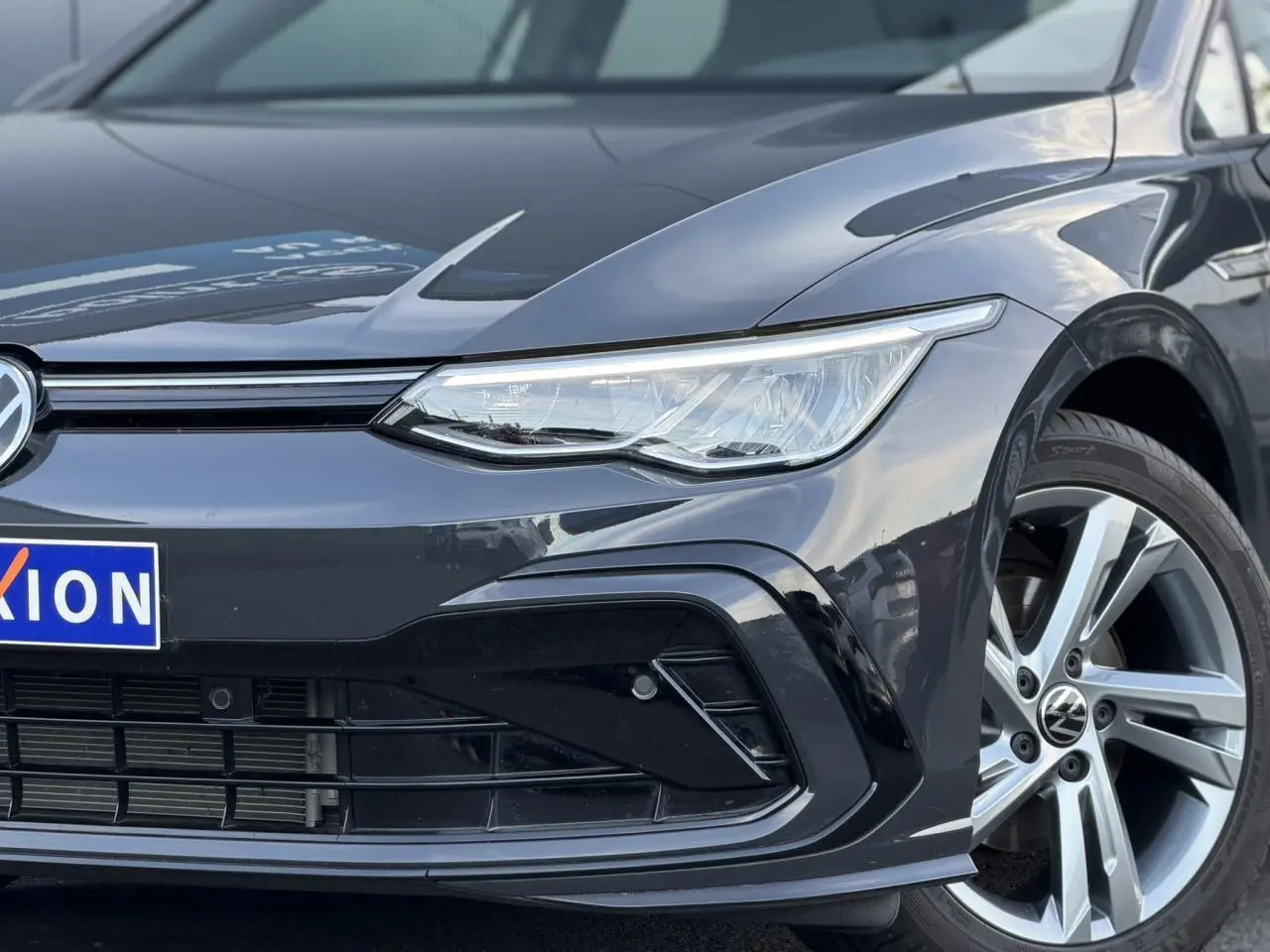Gros plan sur l'avant droit de la Volkswagen Golf 8 R-Line 2024 en Gris Urano avec projecteur LED et jante alliage Valencia.