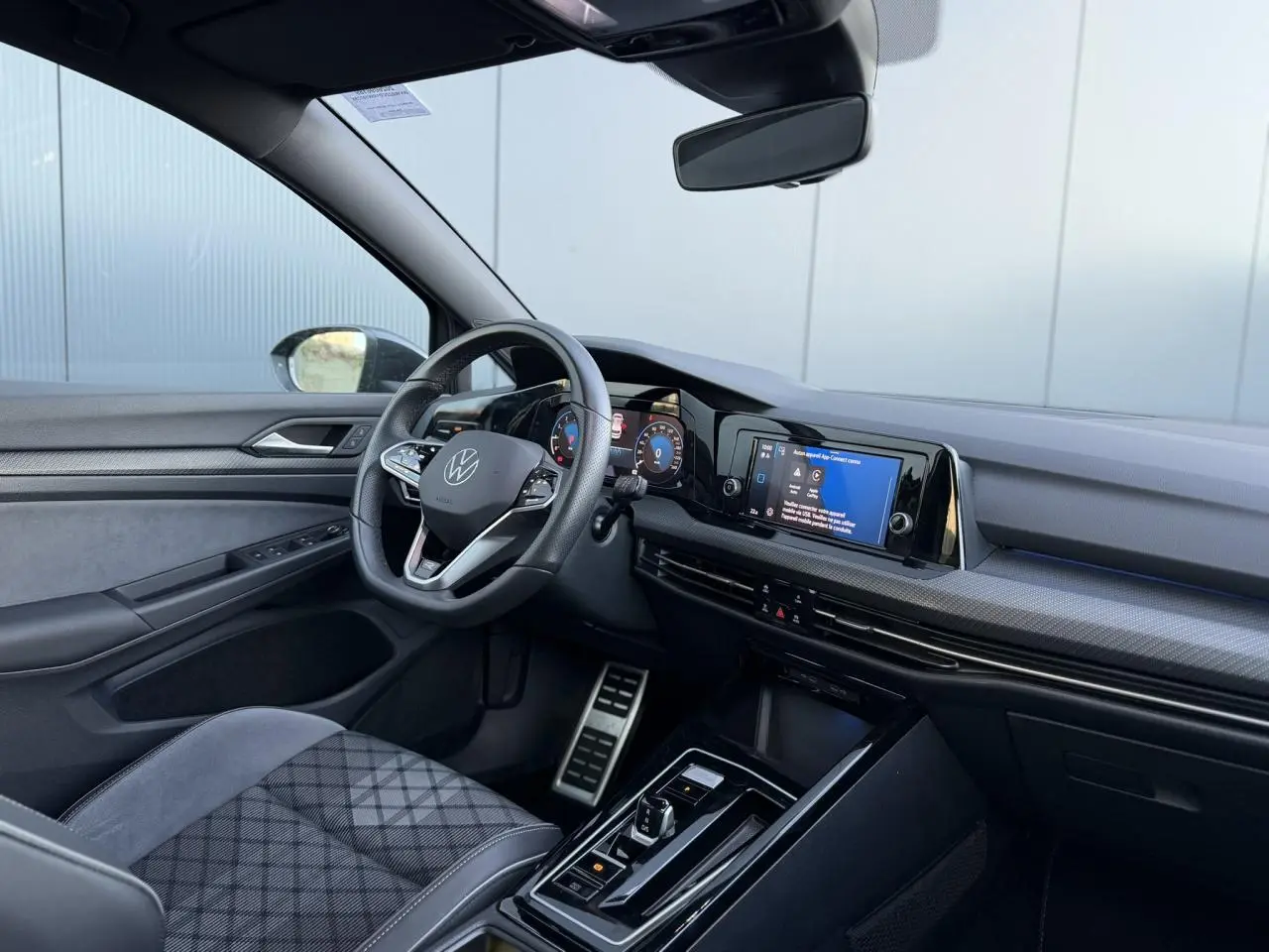 Vue intérieure côté conducteur de la Volkswagen Golf 8 R-Line 2024, avec sellerie tissu gris et tableau de bord numérique.
