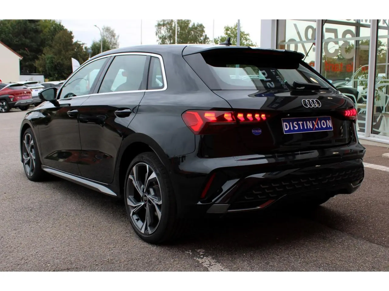 Audi A3 Sportback noir mito metal vue 3/4 arrière droit avec feux arrière LED allumés et jantes 18 pouces graphiques.