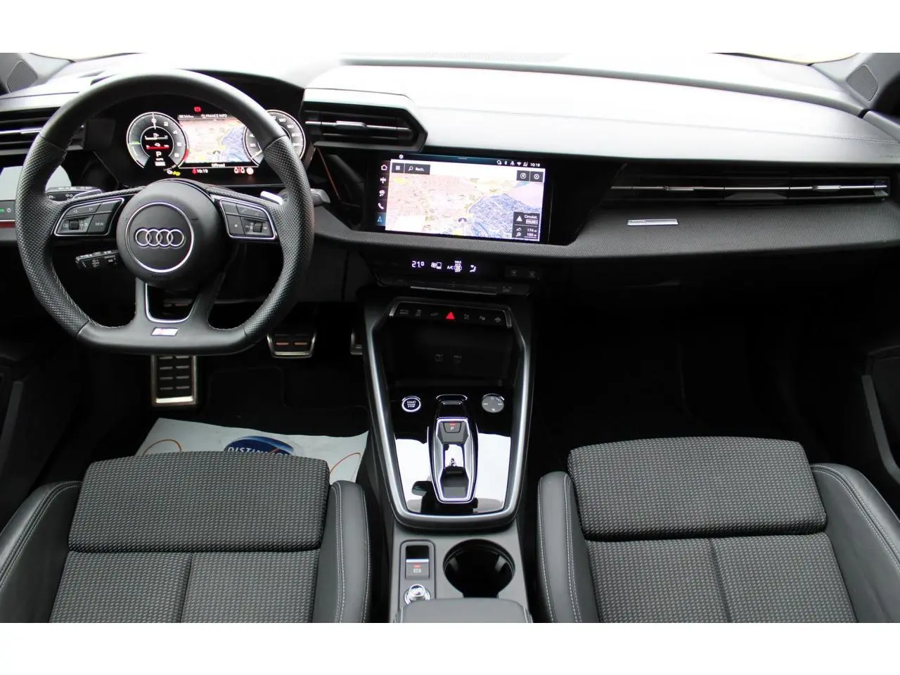 Vue intérieure avant de l'Audi A3 Sportback 2025, tableau de bord noir avec écran tactile et volant cuir multifonctions.