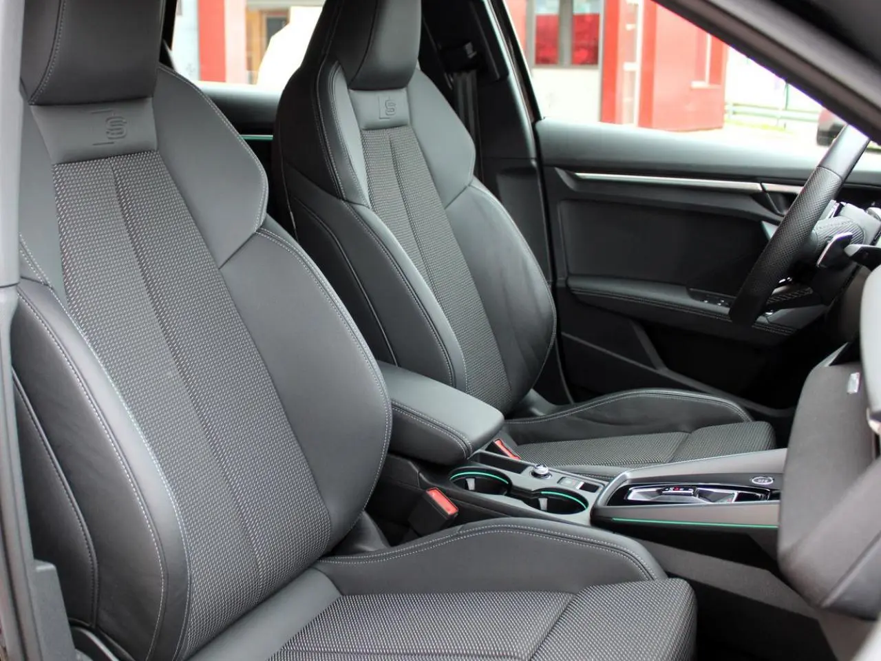 Vue intérieure côté droit des sièges sport noirs avec surpiqûres blanches et accoudoir central de l'Audi A3 Sportback 2025.