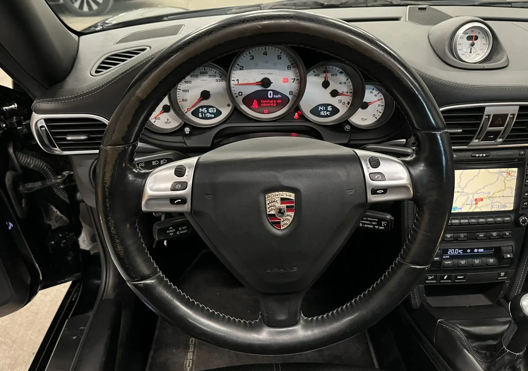 Vue intérieure centrée sur le volant cuir noir et le tableau de bord avec compteurs blancs d'une Porsche 911 Targa 997 Carrera 4S.